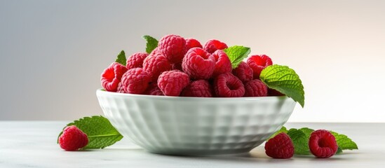 A closeup copy space image of a bowl containing fresh raspberries and mint leaves placed on a light...