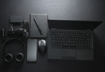 Fototapeta na wymiar Modern black gadgets and accessories. Laptop, camera, smartphone, stereo headphones, notepad on a black background. Working space. Flat lay. Top view