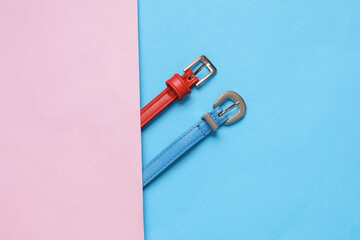 Women's colored leather belts on a blue-pink background. Fashion accessories. Flat lay. Top view
