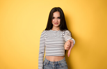 Young girl over isolated yellow background showing thumb down with negative expression