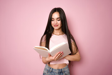 Beautiful smart young girl reading book isolated on pink background