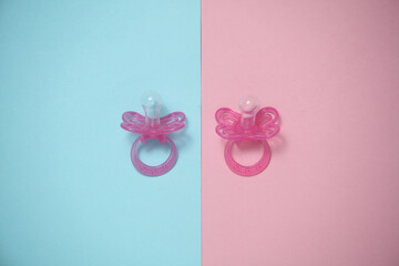 Two baby pacifiers on a blue-pink background. Flat lay