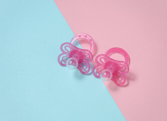 Two baby pacifiers on a blue-pink background. Flat lay