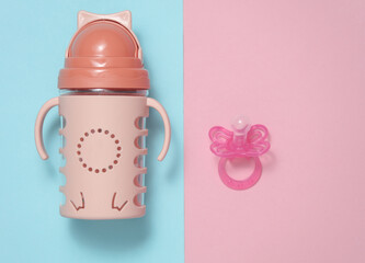 Drinking bowl and Baby pacifier for baby on a blue-pink background. Top view