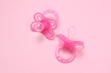 Two baby pacifiers on pink background.
