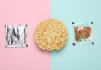Dry instant noodles with spice packets on pink blue background. Top view