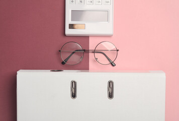 Stylish eyeglasses with calculator and folder on burgundy pink background. Flat lay. Top view. Business concept