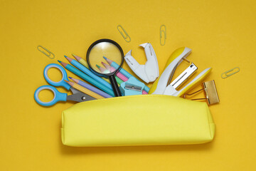 Yellow school pencil case with stationery and school accessories on a yellow background. Back to...