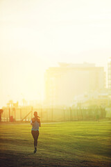 Fototapeta premium Woman, running and back on grass for exercise with mock up space in sky with buildings in city. Girl, person and athlete with training, workout and speed in nature on field for wellness in morning