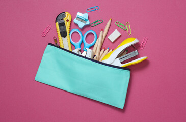 Blue school pencil case with stationery and school accessories on pink background. Back to school...