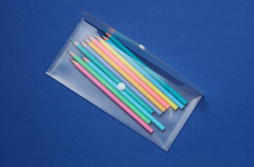 Transparent school pencil case with colored pencils on a blue background