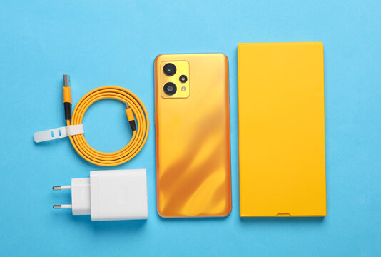 New yellow smartphone with box and accessories on blue background. Modern gadgets, unboxing. Flat lay. Top view - Powered by Adobe