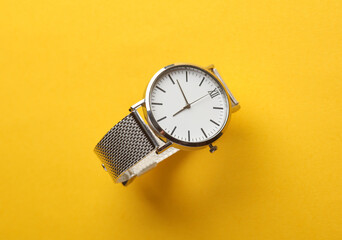 Women's wrist analog watch with metal or silver strap on yellow background