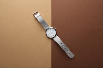 Women's wrist analog watch with metal or silver strap on brown beige background. Flat lay. Top view