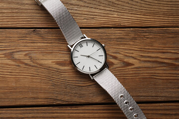 Women's wrist analog watch with metal or silver strap on wooden background.