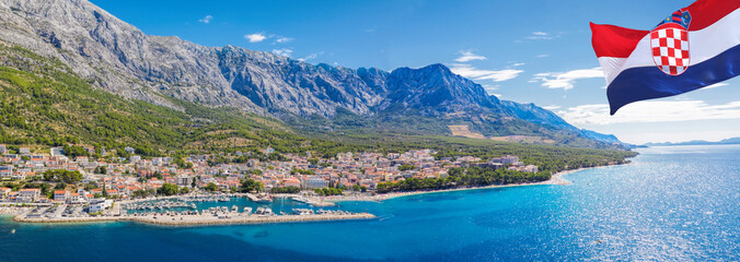 Panorama of Baska Voda town with Croatian flag against mountains and harbor in Makarska riviera,...