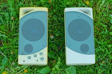 two old small plastic ones with speakers, powerful gray desktop speakers for a computer lie on the green grass outdoors during the day