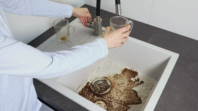 Washing a dirty cup. Clogged drain water in wash basin sink. Dirty sink by coffee. Close up view.
