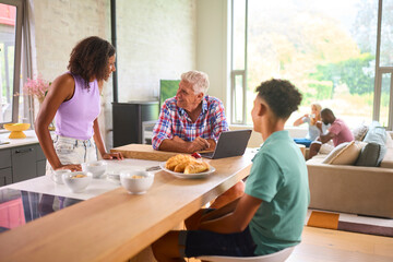 Grandparents With Teenage Grandchildren Indoors At Home Preparing And Eating Breakfast Together