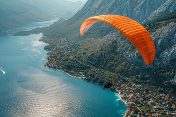 An aerial view captures a paraglider flying above a picturesque coastal town, with a vibrant orange wing against the blue waters