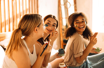 Three charming teenagers of different races apply cosmetic masks to their faces in the bedroom....