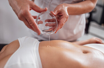 Crop faceless masseuse pouring oil on hand during relaxing massage in spa center