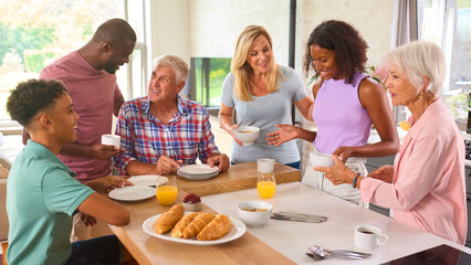 Three Generation Family Indoors At Home Preparing And Eating Breakfast Together