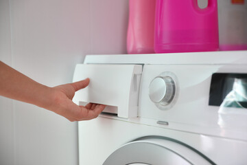 Woman opening detergent drawer of modern washing machine in bathroom, closeup