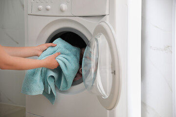 Woman putting dirty laundry into washing machine indoors, closeup