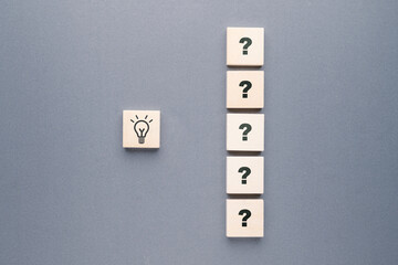 A row of question marks on wooden blocks and a light bulb symbol, many questions lead to the...