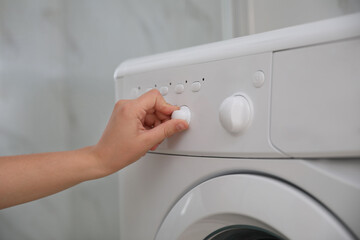 Woman turning on washing machine in bathroom, closeup. Laundry day