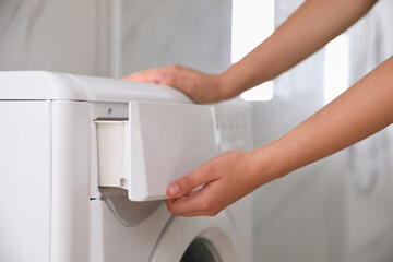 Woman opening detergent drawer of modern washing machine in bathroom, closeup