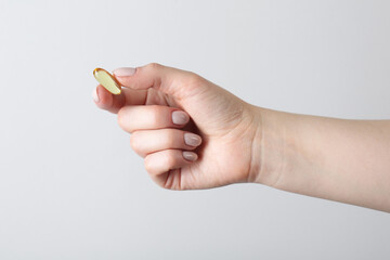 Woman holding vitamin capsule on light grey background, closeup. Health supplement