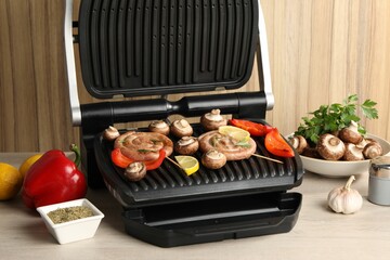 Electric grill with homemade sausages, vegetables and spices on wooden table
