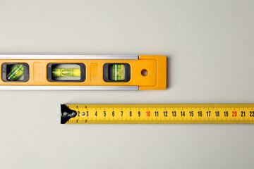 Building level and tape measure on beige background, top view