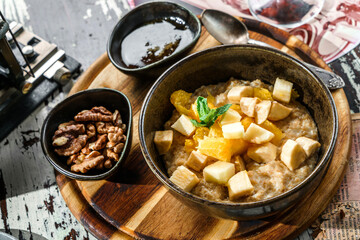 Oatmeal porridge with pieces of fruit, nuts and honey in bowl on wooden background. Healthy...