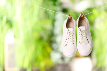 Stylish sneakers drying on washing line against blurred background, space for text