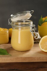 Delicious lemon curd in glass jars, fresh citrus fruit and green leaf on wooden table