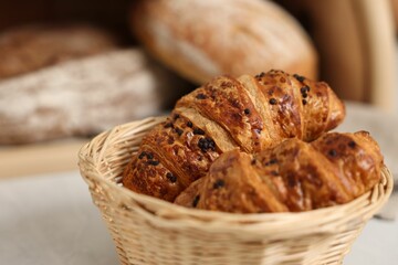 Wooden bread basket with freshly baked loaves and croissants on white marble table in kitchen, closeup. Space for text