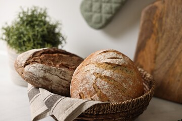 Wicker bread basket with freshly baked loaves on table in kitchen, closeup
