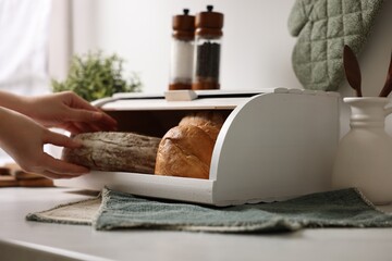 Woman taking loaf from wooden bread basket at white marble table in kitchen, closeup