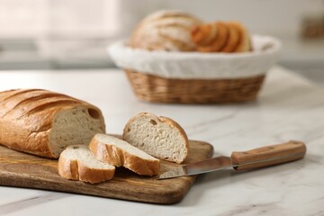 Wicker bread basket with freshly baked loaves and knife on white marble table in kitchen