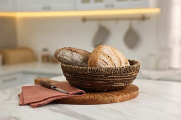 Wicker bread basket with freshly baked loaves on white marble table in kitchen