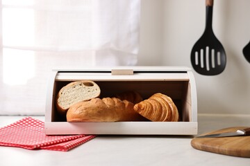 Wooden bread basket with freshly baked loaves on white marble table in kitchen