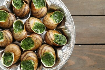 Delicious cooked snails on wooden table, top view. Space for text