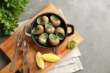Delicious cooked snails in baking dish served on grey textured table, flat lay