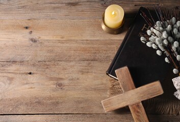 Burning church candle, cross, Bible and willow branches on wooden table, flat lay. Space for text