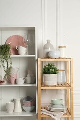 Different clean dishware and houseplants on shelves in cabinet indoors