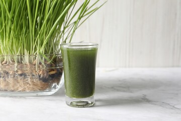 Wheat grass drink in shot glass and fresh sprouts on white marble table, space for text