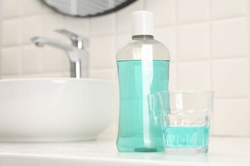 Bottle of mouthwash and glass on white table in bathroom, space for text